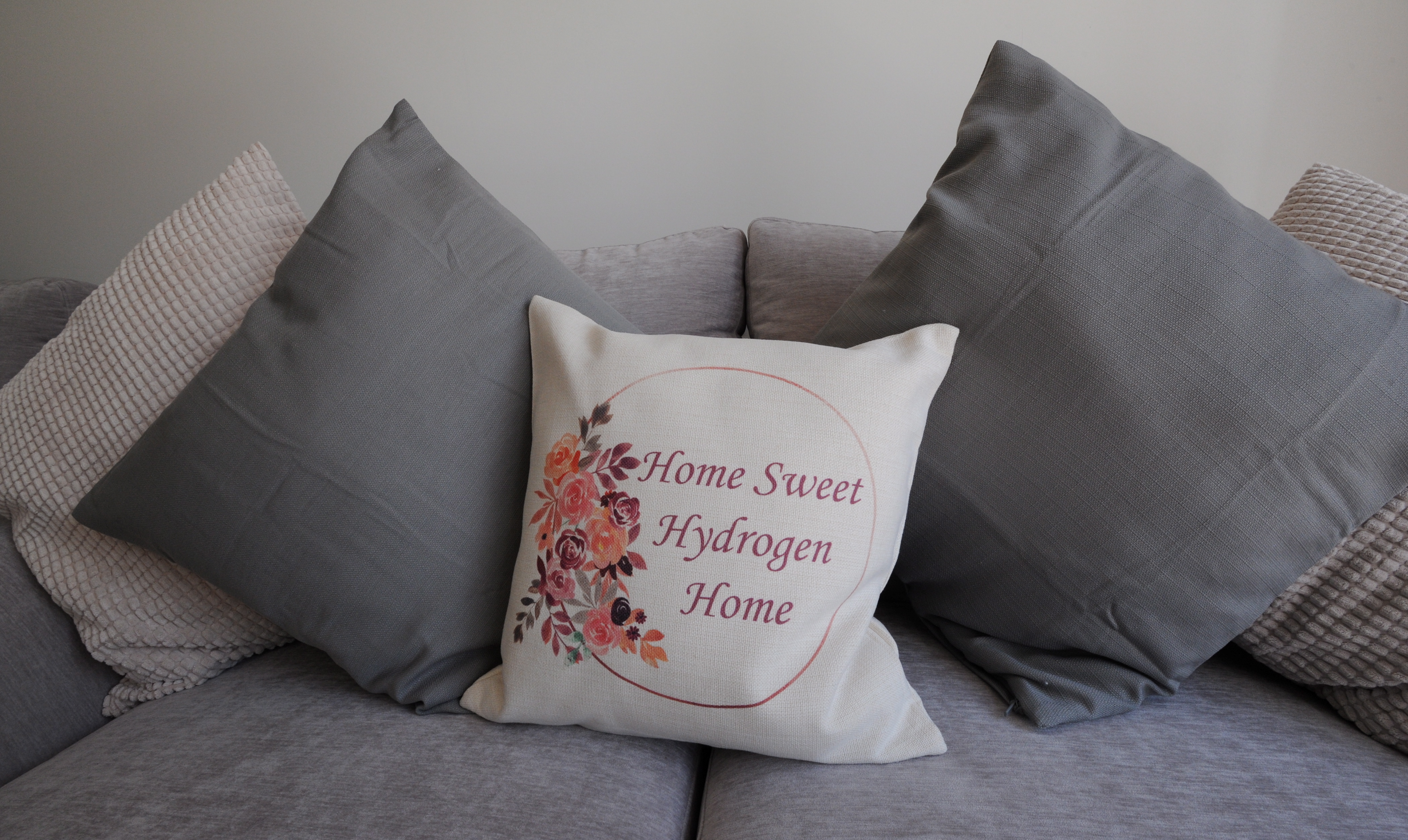 A sofa pillow with "Home Sweet Hydrogen Home" embroidered on it.