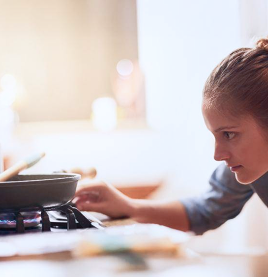 Woman looks down at saucepan on a hob
