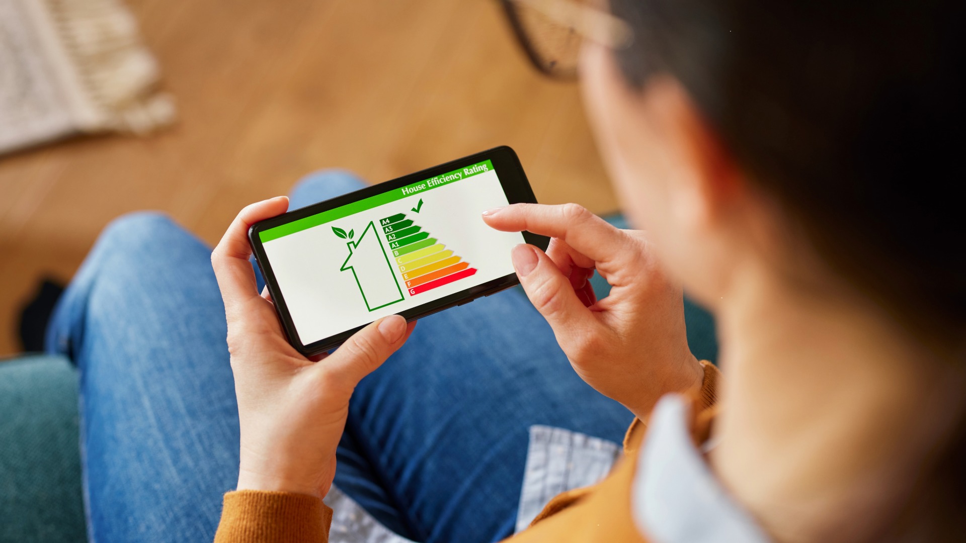 Image is shot looking over shoulder of a women holding a mobile phone with energy efficiency house rating image on the screen.