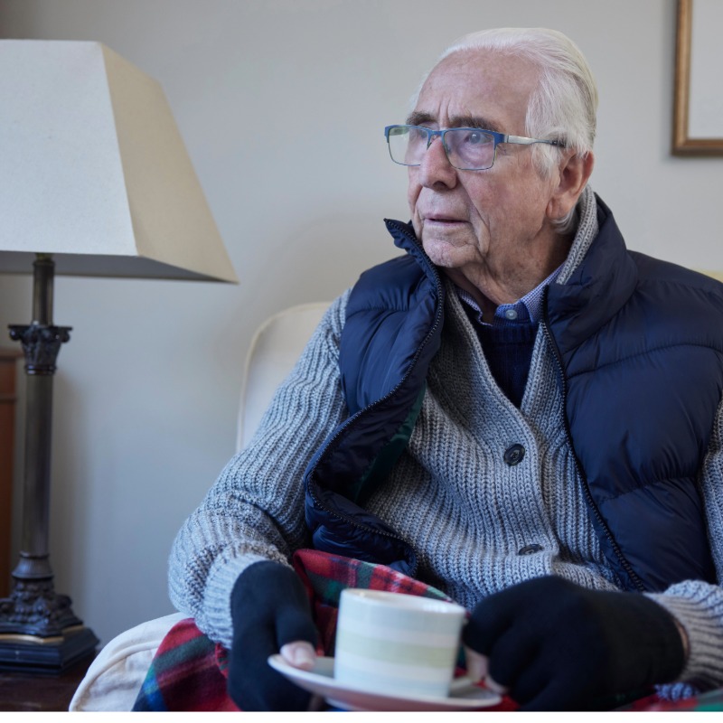Image of a elderly gentleman with blue bodywarmer and gloves on drinking a hot drink for a white cup.