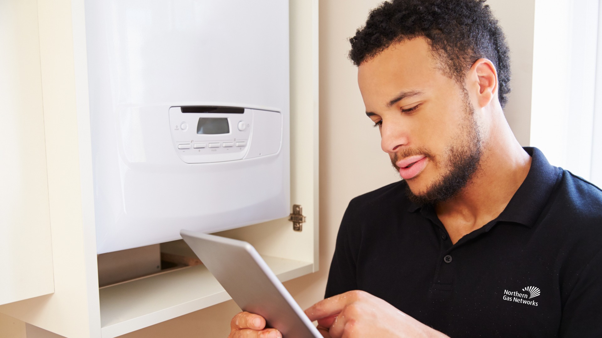 Image of man in blue shirt checking boiler and marking up findings on a tablet.
