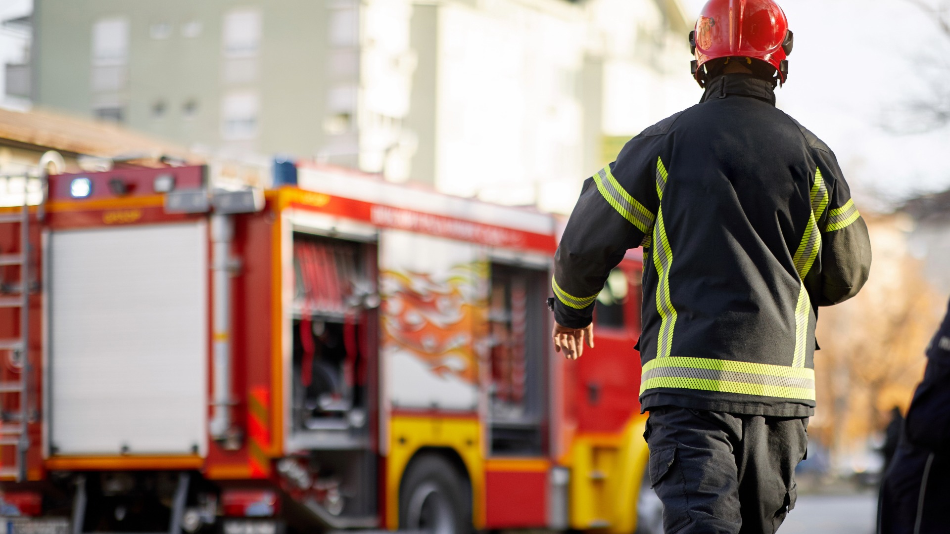Image of back of firefighter walking towards a red fire engine.