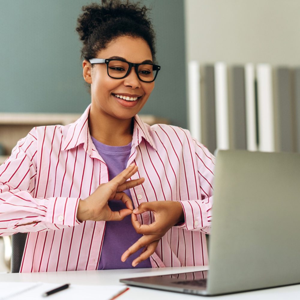Woman wearing pink striped shirt communicating on a video call using British Sign Language.