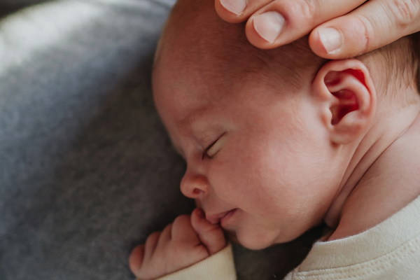 Close up image of new born baby on dad's chest with his hand resting on his child's head as they sleep.