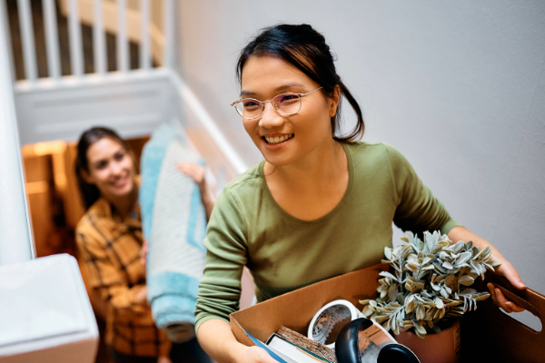 Image of female student moving in and carrying box upstairs.